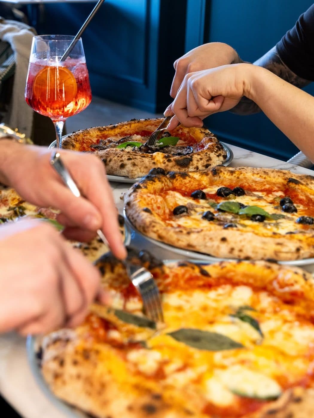 Mains qui se servent une part de pizza autour d'un Spritz